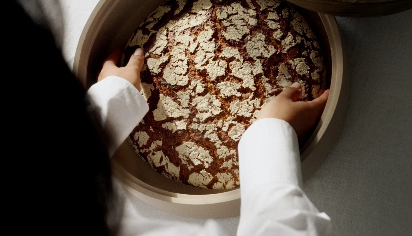 Brot wird von oben in eine Keramikschale gelegt